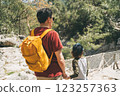 Close-up rear view of tourists school boy and his dad walking a stone footpath in spring forest. Child boy and father wearing casual clothes and yellow backpack while hiking summer greenwood forest 123257363