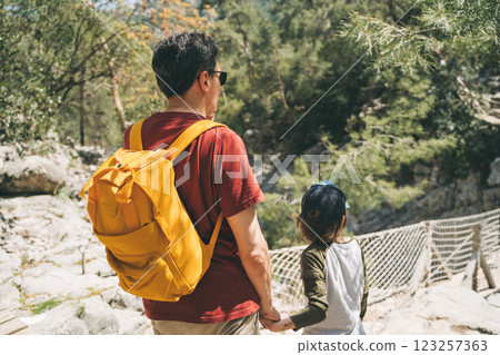 Close-up rear view of tourists school boy and his dad walking a stone footpath in spring forest. Child boy and father wearing casual clothes and yellow backpack while hiking summer greenwood forest 123257363