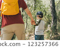 Close-up rear view of tourists school boy and his dad walking a stone footpath in spring forest. Child kid and father wearing casual clothes and yellow backpack hiking in summer greenwood forest 123257366