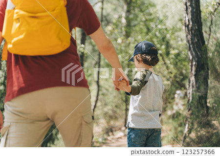 Close-up rear view of tourists school boy and his dad walking a stone footpath in spring forest. Child kid and father wearing casual clothes and yellow backpack hiking in summer greenwood forest Close-up rear view of tourists school boy and his dad walking a stone footpath in spring forest. Child kid and father wearing casual clothes and yellow backpack hiking in summer greenwood forest 123257366