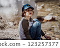 Caucasian school boy sits on a riverside rock in the canyon with mountain cliffs in the background. Kid child taking a rest on a boulder near mountain river bank 123257377