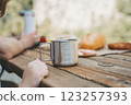 School boy kid child having a family picnic and looking at coffee, tea metallic mug that stands on a wooden table with bread and vegetables 123257393