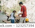 Father dad pours hot coffee tea from thermos into the mug on a family picnic in the mountains. Child school boy kid is watching his dad filling the cup with hot beverage 123257394