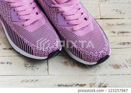 On the wooden surface is a pair of pink sneakers with pink laces 123257867