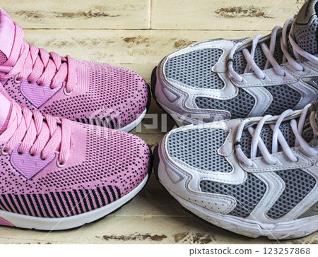 A pair of pink women's sneakers and a pair of white men's sneakers on a wooden surface 123257868