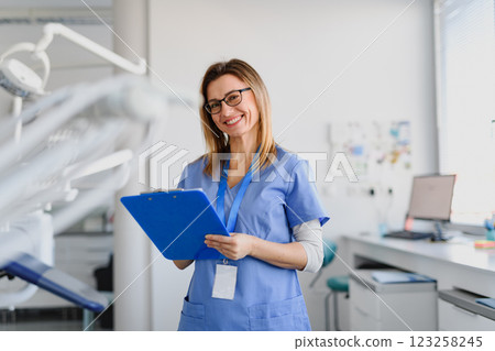 Friendly nurse writing notes in patients records, standing a modern medical clinic. Friendly nurse writing notes in patients records, standing a modern medical clinic. 123258245