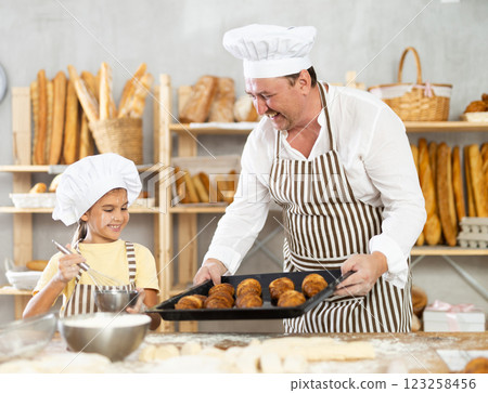 Family bakery - father showing girl baked hot croissants on tray 123258456