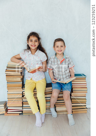 Boy And Girl Sitting On Stacks Of Books In Library 123259251