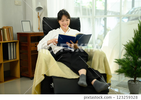 Relaxed young woman reading a book on a comfortable armchair Relaxed young woman reading a book on a comfortable armchair 123259328