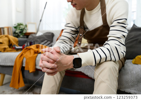 Cropped shot of exhausted man sitting on couch in messy living room Cropped shot of exhausted man sitting on couch in messy living room 123259373