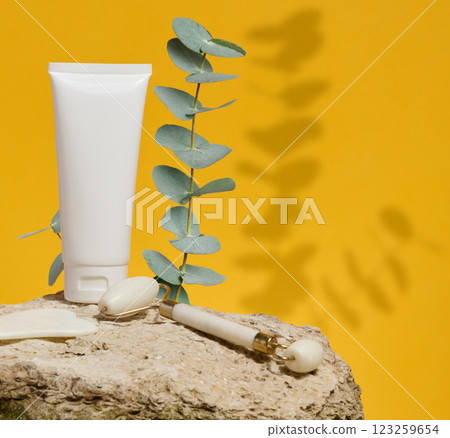 White tube, jade gouache massager and massage jade roller on a yellow background 123259654