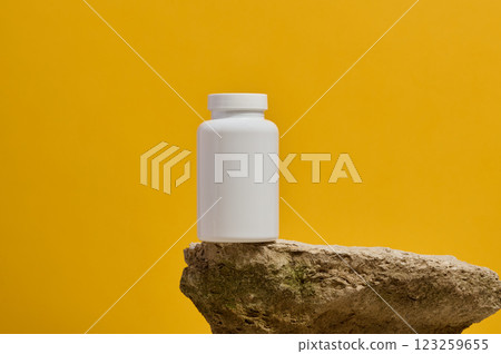 White plastic medicine jar on stone, yellow background. Mock up 123259655