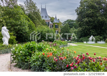 A picturesque view of a historic brick mansion with a round tower, pointed roof, and arched windows, surrounded by lush greenery, manicured gardens, and a peaceful, cloudy sky. A picturesque view of a historic brick mansion with a round tower, pointed roof, and arched windows, surrounded by lush greenery, manicured gardens, and a peaceful, cloudy sky. 123259834