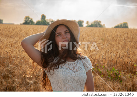 Young woman in lace dress and straw hat posing in a golden wheat field at sunset. Harvesting concept Young woman in lace dress and straw hat posing in a golden wheat field at sunset. Harvesting concept 123261340