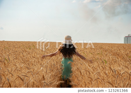In the middle of an agricultural wheat field, a young girl stands with her back turned. Harvesting concept 123261366