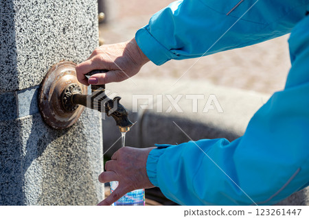 A woman fills a bottle of water from a tap on the street, hands closeup 123261447