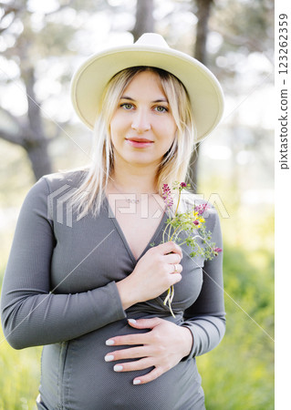 Beautiful pregnant woman in hat and dress walking in the forest. Woman expecting baby born. 123262359