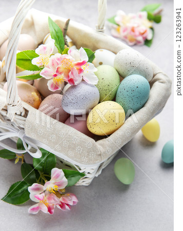Pastel colored easter eggs overflowing from a white wicker basket decorated with spring flowers 123263941