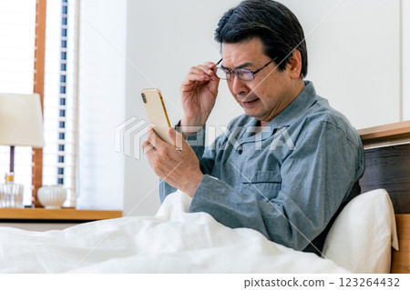 Middle-aged man with glasses using smartphone in bed 123264432