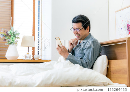 戴眼鏡的中年男子在床上使用智慧型手機 123264433