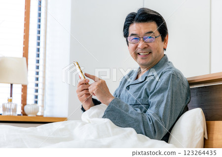 戴眼鏡的中年男子在床上使用智慧型手機 123264435