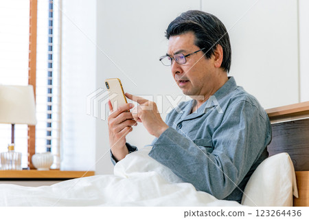 戴眼鏡的中年男子在床上使用智慧型手機 123264436