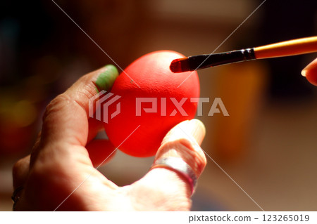 A woman's hand paints an Easter egg. Preparing Easter decorations on Multicolor background. 123265019