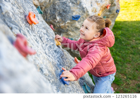 Little girl climbing an artificial climbing wall in a playground, developing strength and coordination Little girl climbing an artificial climbing wall in a playground, developing strength and coordination 123265116