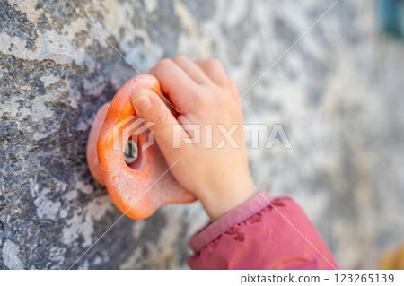 Close up view of hand of little girl climbing an artificial climbing wall in a playground, developing strength and coordination Close up view of hand of little girl climbing an artificial climbing wall in a playground, developing strength and coordination 123265139