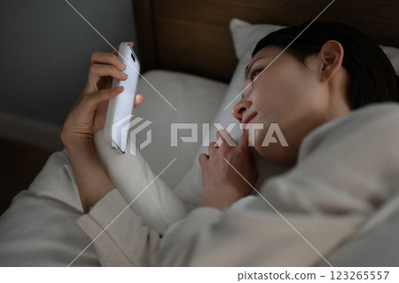 A woman using a smartphone in bed A woman using a smartphone in bed 123265557