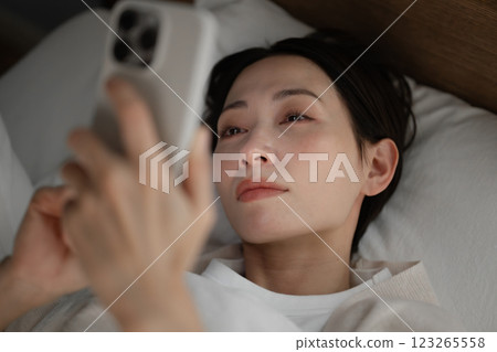 A woman using a smartphone in bed A woman using a smartphone in bed 123265558
