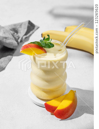 Frozen smoothie with mango and banana in a glass on a light background with tropical fruit slices 123265620
