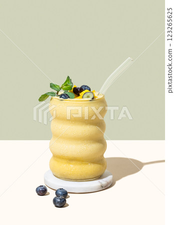 Smoothie with mango, banana and blueberry in a glass on a yellow and green background 123265625
