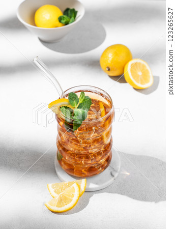 Iced tea with lemon, ice and mint in a glass on light background with shadow and citrus fruits. Iced tea with lemon, ice and mint in a glass on light background with shadow and citrus fruits. 123265627