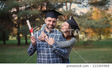 A joyful couple enthusiastically celebrates their graduation outdoors, showcasing immense happiness and love 123265909
