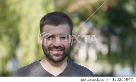A cheerful man with a wellgroomed beard stands outdoors, surrounded by lush greenery, enjoying natures beauty A cheerful man with a wellgroomed beard stands outdoors, surrounded by lush greenery, enjoying natures beauty 123265947