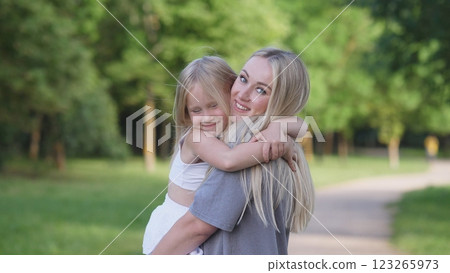 In a beautiful, lush green park, a heartwarming embrace between a loving mother and her joyful daughter occurs 123265973