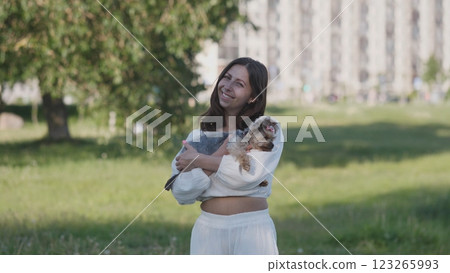 A woman joyfully holds a small dog in a sunny field that is beautifully surrounded by natures splendor 123265993