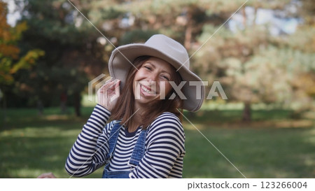A joyful woman wearing a chic hat enjoys the beauty of nature, radiating her happiness amidst lush greenery A joyful woman wearing a chic hat enjoys the beauty of nature, radiating her happiness amidst lush greenery 123266004