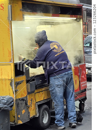 New York street vendor cooks fresh food in a vibrant yellow halal food cart on a city sidewalk, epitomizing urban street food culture with a bustling environment and parked cars nearby 123266204
