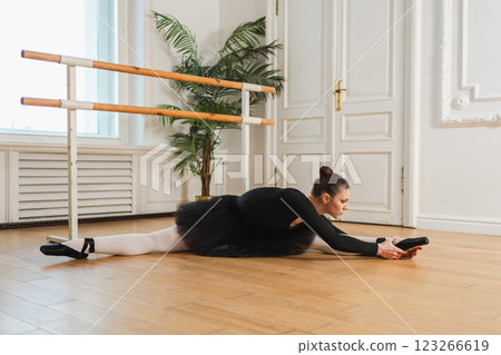 Young ballerina in tutu skirt stretching practicing ballet positions dancing in dance class. Young classical dancer woman in dance studio. Ballet class training Ballet school concept 123266619