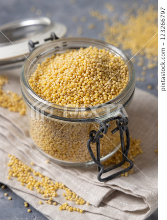 Glass jar of raw uncooked yellow millet grain on napkin on gray table closeup. Ancient food Glass jar of raw uncooked yellow millet grain on napkin on gray table closeup. Ancient food 123266797