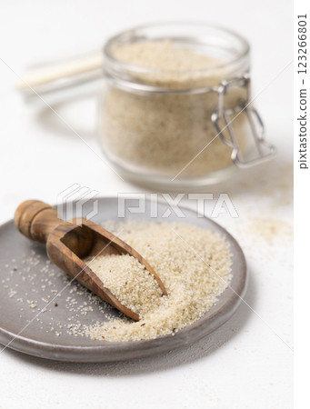 Raw uncooked fonio seeds on grey plate with a wooden scoop on white table closeup. African cereal 123266801