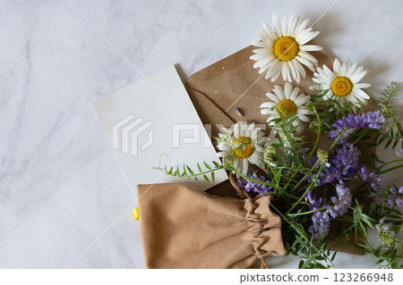 Florist at work: a pretty woman prepares a summer bouquet of white gypsophila on a gray desk. Kraft paper, scissors, greeting envelope on the table. View from above. The composition is flat. 123266948