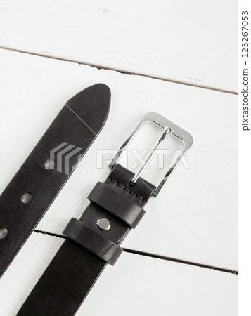 Black genuine leather belt on a white wooden background. Black genuine leather belt on a white wooden background. 123267053
