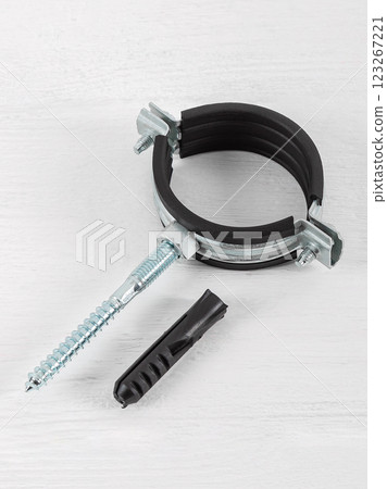 Clamp with a rubber gasket and fasteners on a white wooden background. Pipe holder, protection against water leaks. 123267221