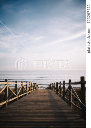 A wooden boardwalk extends toward the sea, illuminated by the warm sunset glow. The calm waters and A wooden boardwalk extends toward the sea, illuminated by the warm sunset glow. The calm waters and 123267511