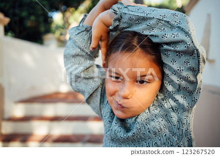 A young girl playfully stretches her arms and makes a funny face, enjoying a sunny day outdoors 123267520