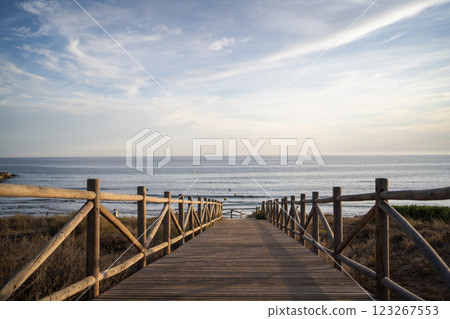 A wide-angle view of a peaceful beach and ocean as the sun sets behind distant hills, casting a warm A wide-angle view of a peaceful beach and ocean as the sun sets behind distant hills, casting a warm 123267553
