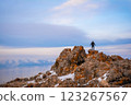 A man stands on the top of a cliff. A traveler stands on the top of a mountain and looks at the sea. Beautiful documentary landscape. Beautiful nature with a rocky mountain and a lake	 123267567